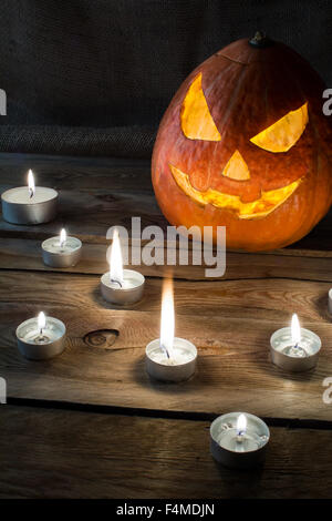 Zucca di Halloween sorridente jack-o-lantern e candele accese sul legno scuro, sfondo verticale, copyspace Foto Stock