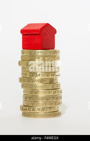 Pila di British una libbra di monete con un monopolio di legno-casa in stile seduti sulla parte superiore Foto Stock