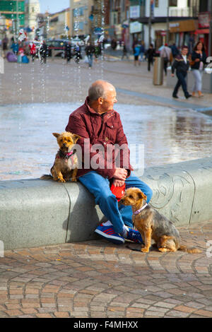 Un anziano seduto su una panchina con i suoi due cani in St Johns Square, Blackpool, Lancashire, Regno Unito Foto Stock