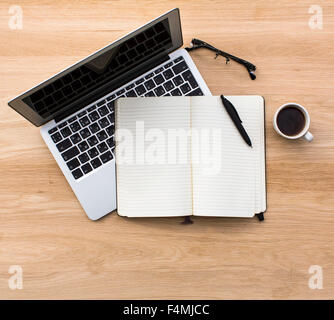 Laptop, notebook con penna, occhiali e la tazza di caffè. Vista superiore, steso su un tavolo di legno. Foto Stock