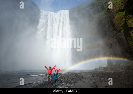 La famiglia in rainbow sotto 60m-alta cascata Skogafoss, Skogar, Sudhurland, Islanda. Foto Stock