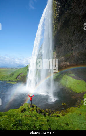 Persona e rainbow sotto 60m-alta cascata Seljalandsfoss, Sudhurland, Islanda. Foto Stock