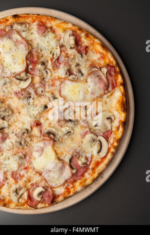La Pizza sul piatto di legno con funghi, prosciutto affumicato e mozzarella Foto Stock