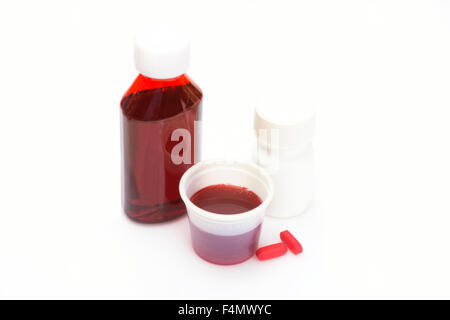 Liquido di medicina a freddo in tazza wirh flacone di farmaco e pillole di rosso. Foto Stock