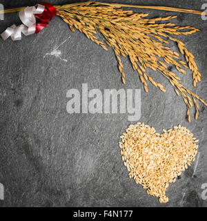 Nella foto una spiga di grano e un cuore formato da grani di riso su sfondo di pietra. Foto Stock