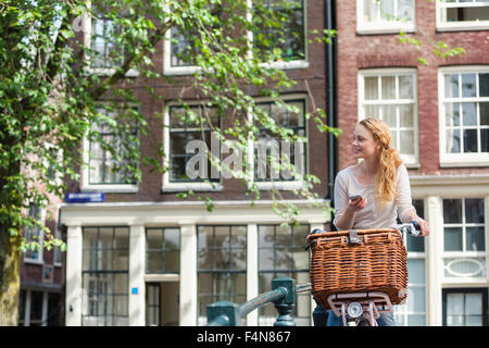 Paesi Bassi, Amsterdam, donna con la bicicletta e telefono cellulare nella città Foto Stock