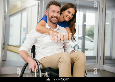 Uomo in carrozzella con la sua fidanzata, abbracciando felicemente Foto Stock