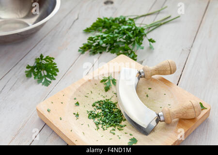 Prezzemolo tritato su una scheda con la mezzaluna Foto Stock