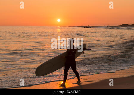 Surfer camminando lungo la spiaggia al tramonto, Cape May New Jersey USA Foto Stock