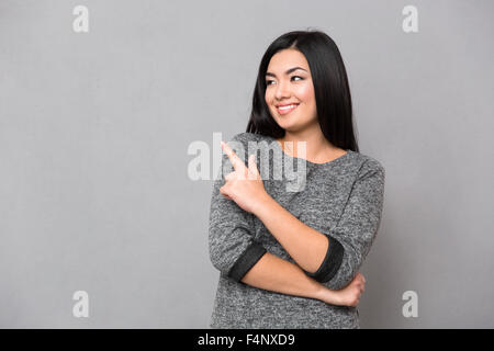 Ritratto di una donna sorridente puntare il dito lontano su sfondo grigio Foto Stock