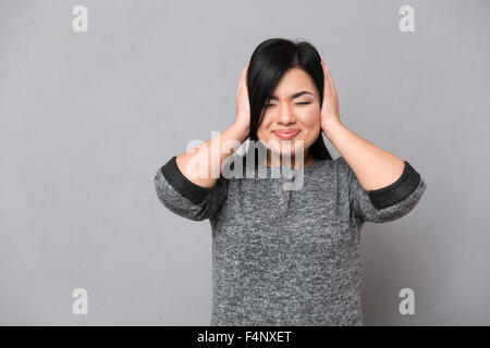Ritratto di una donna giapponese che copre le sue orecchie su sfondo grigio Foto Stock