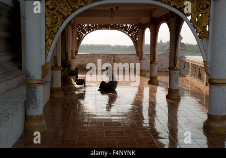 Un uomo birmano si siede zampe croce pregare presso un santuario buddista in un tempio sulle rive del Fiume Ayeyarwady Mandalay Myanmar Foto Stock