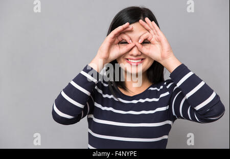 Giovani belle sorridenti donna nel ponticello striato guardando la telecamera rendendo le mani come una maschera sul viso Foto Stock