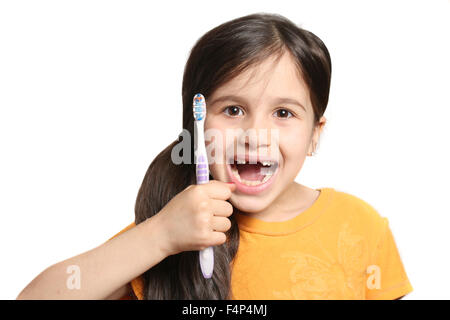 Poco di sette anni ragazza mostra grande sorriso assenti top denti frontali e tenendo premuto uno spazzolino da denti su sfondo bianco Foto Stock