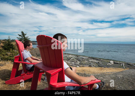 Una coppia di fratelli adolescenti seduti su sedie fornite dai parchi Canada sedia rossa Programma, Isola di Vancouver Foto Stock