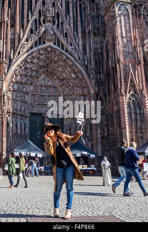 Donna asiatica tenendo autoritratto con lo smartphone sul bastone selfie davanti alla Cattedrale di Nostra Signora di Strasburgo, Francia Foto Stock