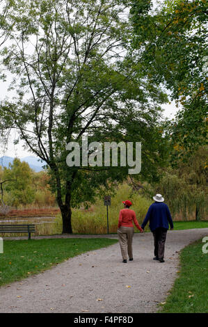 Anziano uomo e donna camminando mano nella mano lungo un percorso nel Parco di Gerico, Vancouver, BC, Canada Foto Stock