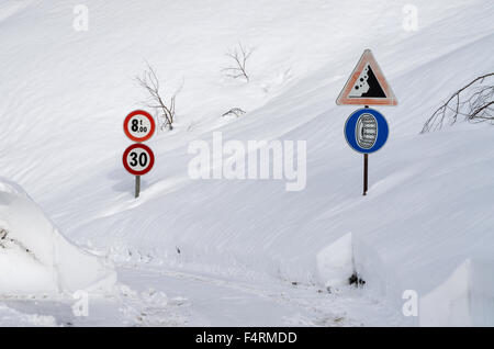 Road sign on a mountain road partially covered by the snow Foto Stock