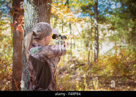 Giovane donna di puntamento di un fucile in una zona boscosa di indossare il camuffamento. Foto Stock