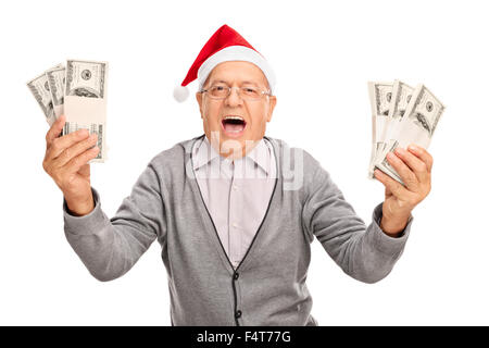 Senior estatica gentiluomo con Santa hat holding alcune pile di denaro e guardando la telecamera isolata su sfondo bianco Foto Stock