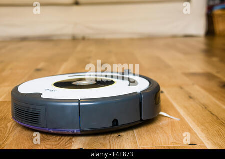 Un iRobot Roomba robotico di aspirapolvere pulizia di un soggiorno in legno il pavimento della camera Foto Stock