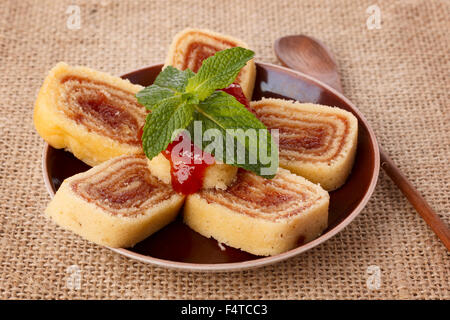 Bolo de rolo (swiss roll, roll cake) dessert brasiliano sulla piastra marrone su un letto di sacco. Messa a fuoco selettiva Foto Stock