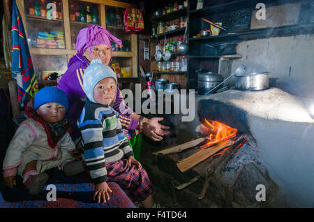 Donna nepalese con i suoi 2 bambini seduti al camino in cucina Foto Stock