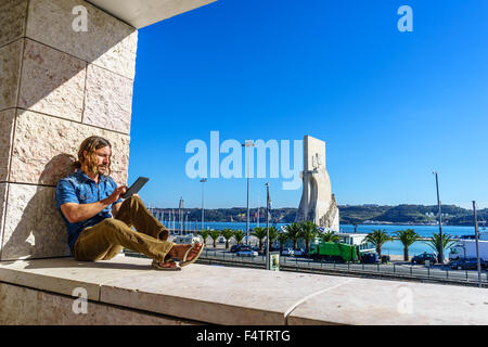 Uomo di legge da una tavoletta elettronica di fronte all'icona portoghese, Monumento alle Scoperte Padrao dos Descobrimentos. Foto Stock