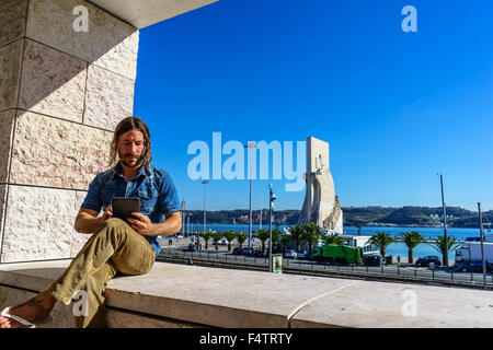 Uomo di legge da una tavoletta elettronica di fronte all'icona portoghese, Monumento alle Scoperte Padrao dos Descobrimentos. Foto Stock