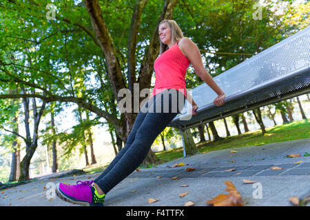 Un accoppiamento femmina di runner si prende una pausa per allungare su una panchina nel parco. Parco Urbano impostazione. Foto Stock