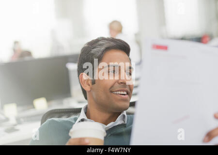 Imprenditore sorridente a bere caffè e la revisione di documenti cartacei Foto Stock