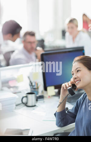 Sorridente imprenditrice parlando al telefono alla scrivania in ufficio Foto Stock