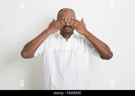 Ritratto di maturo business casual uomo indiano gli occhi coperti, in piedi su sfondo semplice con l'ombra. Foto Stock