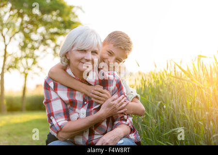 Ritratto sorride la Nonna e nipote abbracciando vicino rurale soleggiato Campo di grano Foto Stock
