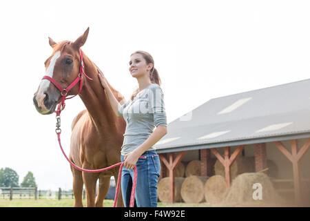 Donna sorridente con cavallo al di fuori del fienile rurale Foto Stock