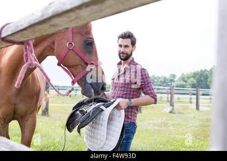 L'uomo rimozione sella da cavallo in pascolo rurale Foto Stock
