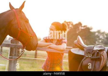 Donna che guarda a cavallo al pascolo rurale recinzione Foto Stock