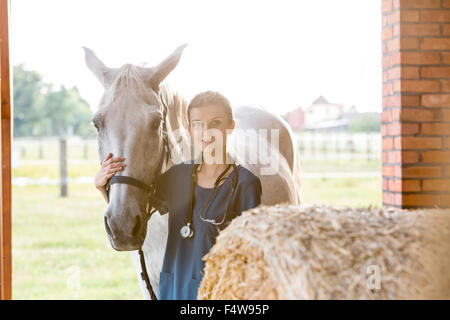 Ritratto sorridente veterinario con cavallo nel fienile Foto Stock