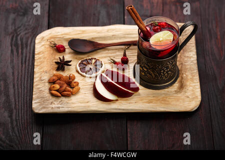 Hot Toddy (vin brulé, punch) con mele e rosa canina servita su legno rustico vassoio con mandorle scure su un tavolo di legno Foto Stock