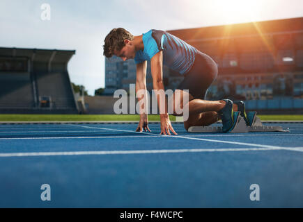 Giovane atleta alla posizione di partenza pronta per iniziare una corsa. Runner maschio pronto per l'esercizio sportivo su autodromo con sun flare. Foto Stock