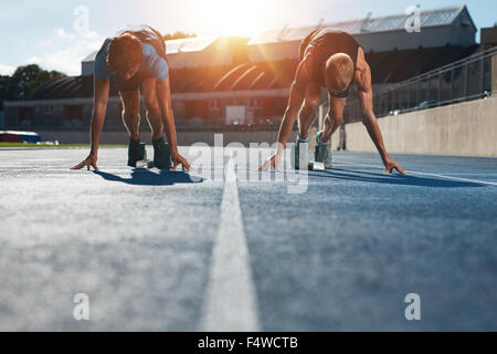 Velocisti in blocchi di partenza pronto per la gara . Gli atleti a posizione di partenza su Athletics Stadium race track con sun flare. Foto Stock