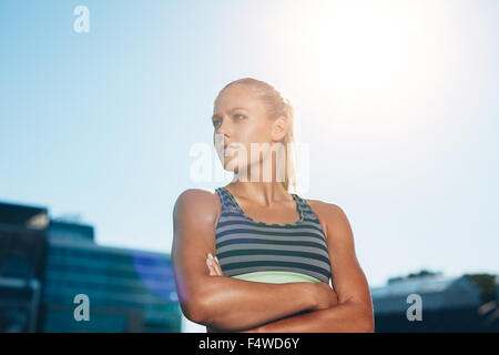 Ritratto di un fiducioso giovane runner in piedi che guarda lontano con le braccia incrociate. Muscoloso atleta femminile in all'aperto stadium on Foto Stock