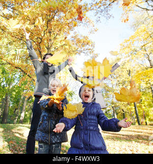 La famiglia felice a giocare con l'autunno foglie di acero in posizione di parcheggio Foto Stock