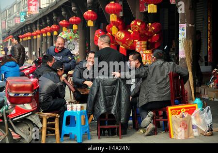 Jun Le, Cina: un gruppo di uomini a giocare a carte di fronte a un negozio con righe di tessuto rosso lanterne per l'Anno Nuovo Cinese Foto Stock