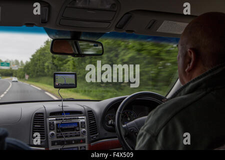 Driver maschio utilizzando un navigatore satellitare (Satellite Navigation Device) su una strada principale nel Regno Unito Foto Stock