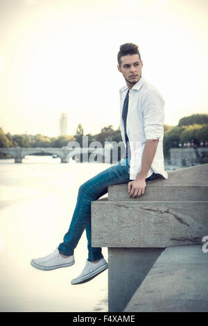 Ritratto di vita contemplativa marrone chiaro pelose giovane uomo che indossa una camicia bianca accanto al pittoresco fiume o lago, guardando lontano per una s Foto Stock