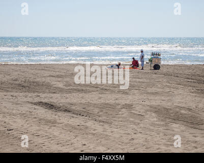 Due venditori ambulanti con un fornitore di vassoio sono offrire i loro prodotti ai turisti che giace sulla spiaggia deserta di Lido di Ostia (Roma, Italia) Foto Stock
