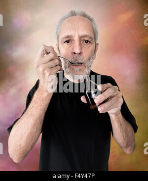 Un uomo maturo è bere un cucchiaio di tosse sciroppo per curare il suo mal di gola e bronchiti Foto Stock