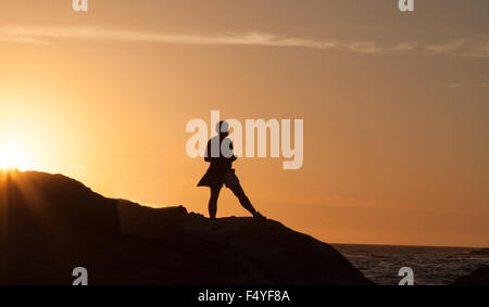 Silhouette di una donna in piedi di fronte al tramonto della linea costiera della California. Foto Stock