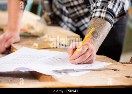 Carpenter piani e progetti scrive a disegni in officina Foto Stock